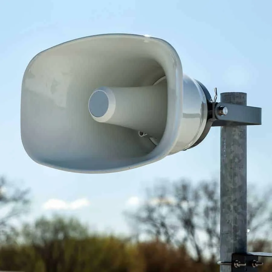 Grey PA horn loudspeaker on a galvanised pole against a blue sky