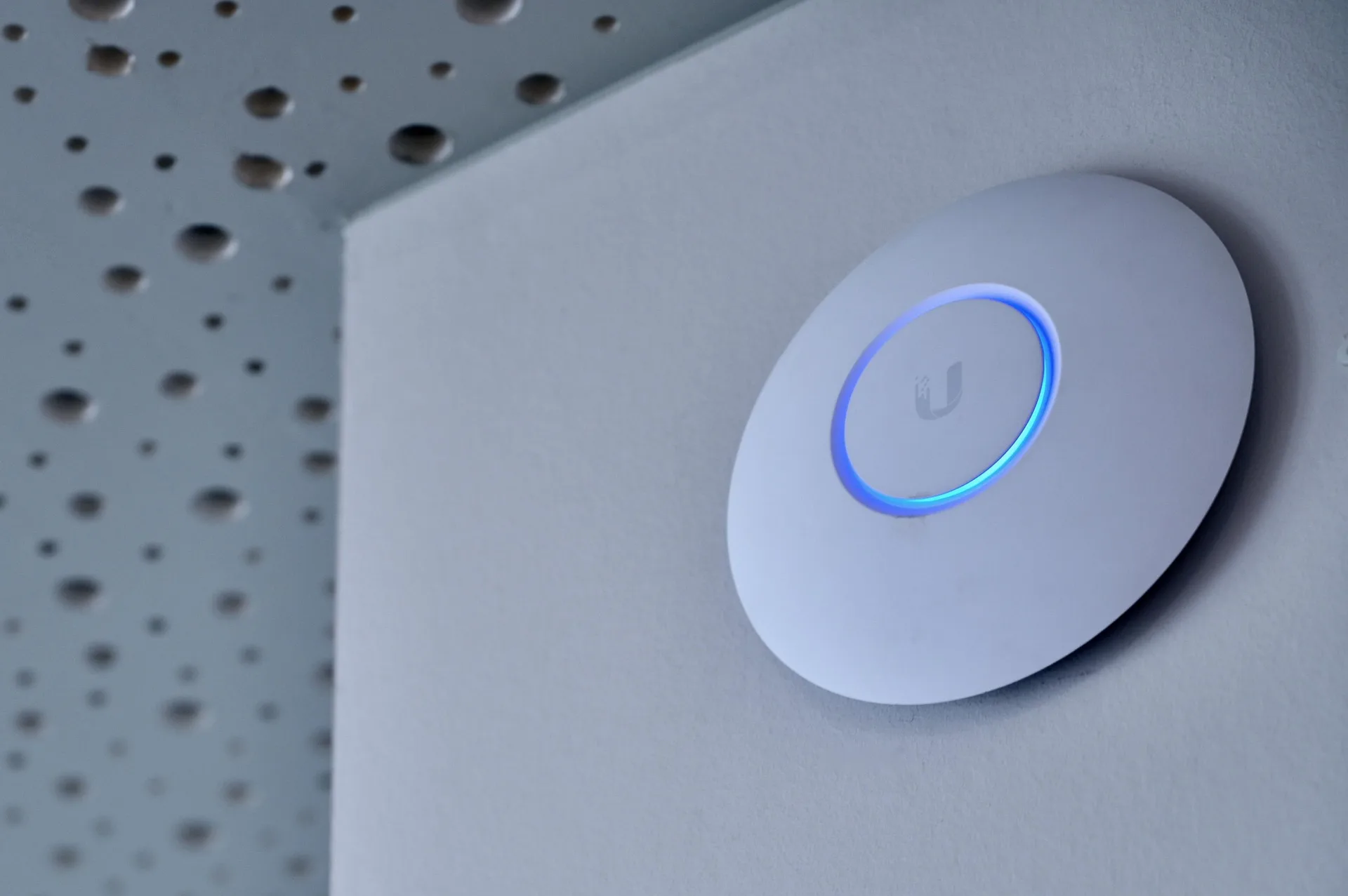 Ceiling-mounted UniFi wireless access point glowing blue